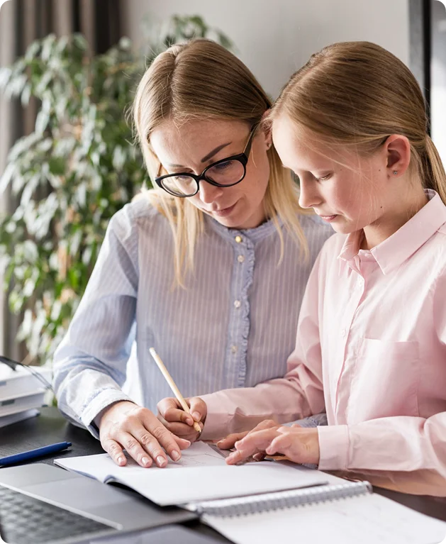 Een lerares of moeder met een bril helpt een jong meisje gefocust met haar huiswerk aan een bureau met een laptop.